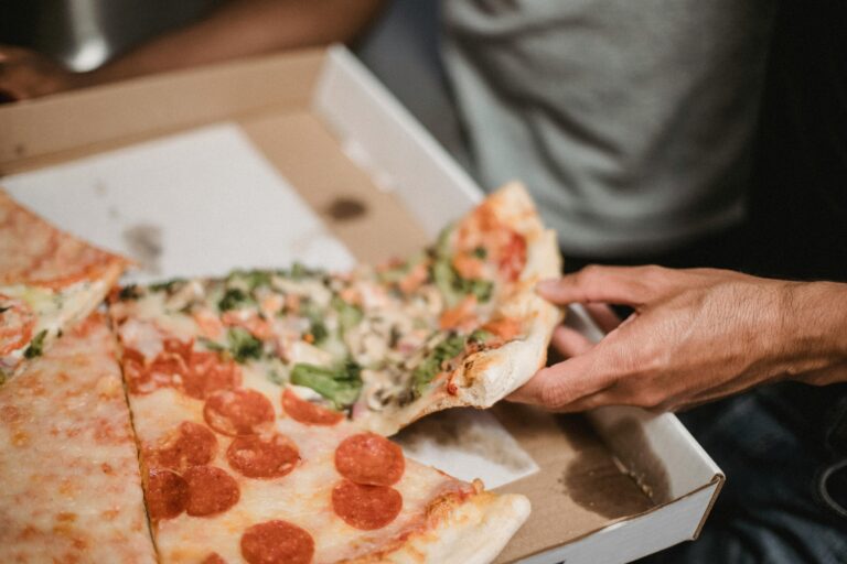 A close-up of a hand grabbing a slice from a pizza box with various toppings.