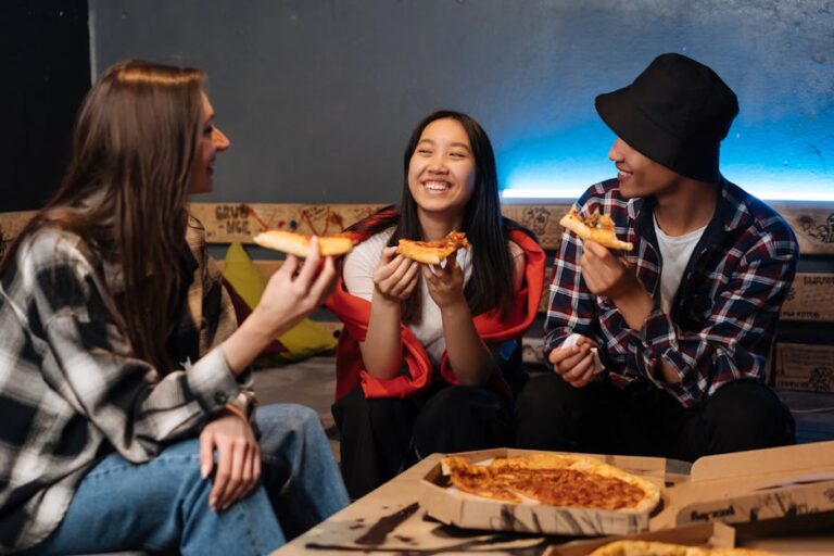 Three teenagers laughing and enjoying pizza together indoors, creating a joyful and friendly atmosphere.